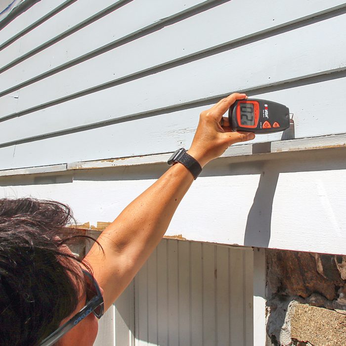 Man using a moisture meter on the side of a house to ensure it's completely dry.